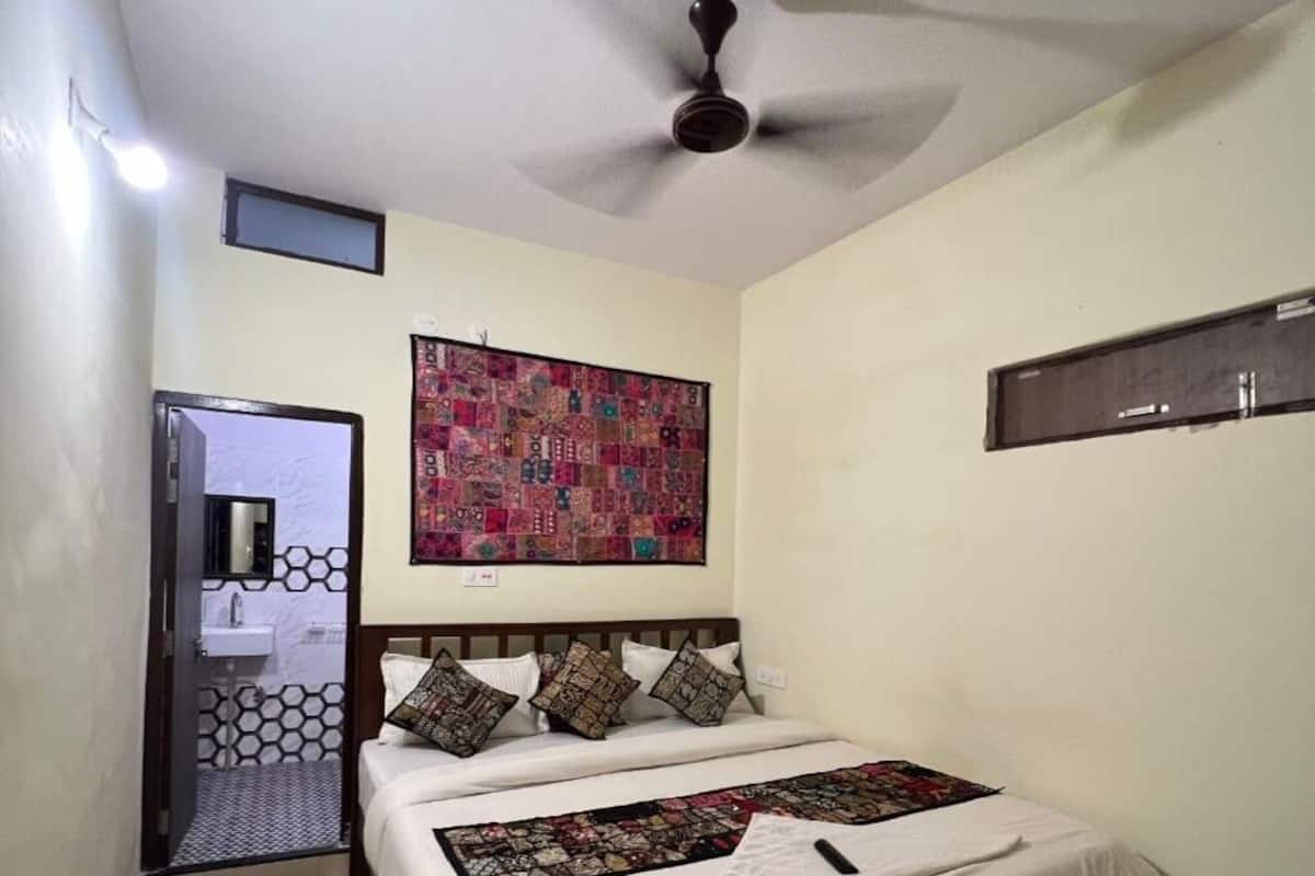 A bedroom with a bed, a ceiling fan, a wall-mounted quilt, and a door leading to a bathroom.
