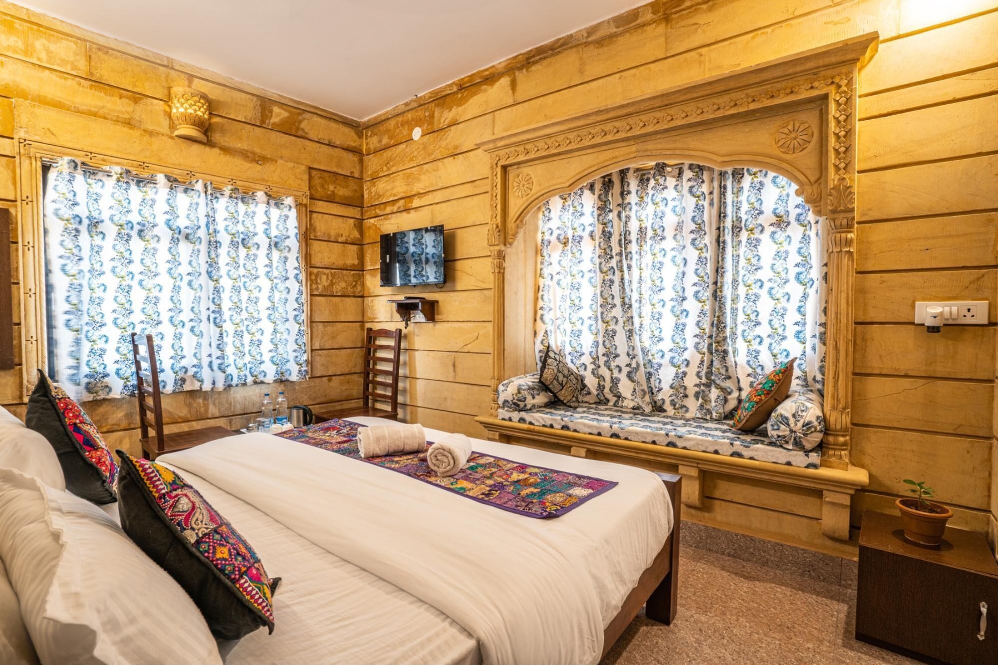A room with a large bed, a window seat with a view, and a television on the wall.