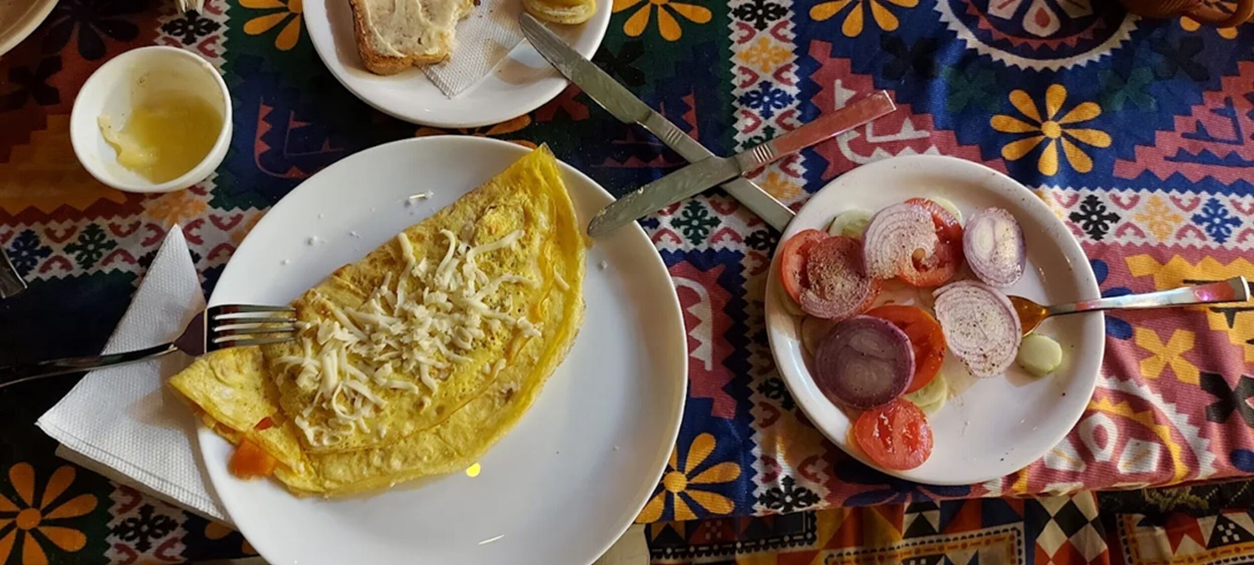 Une table mise pour le petit-déjeuner avec une omelette, une assiette de tomates et d’oignons en tranches, et une tasse de café.