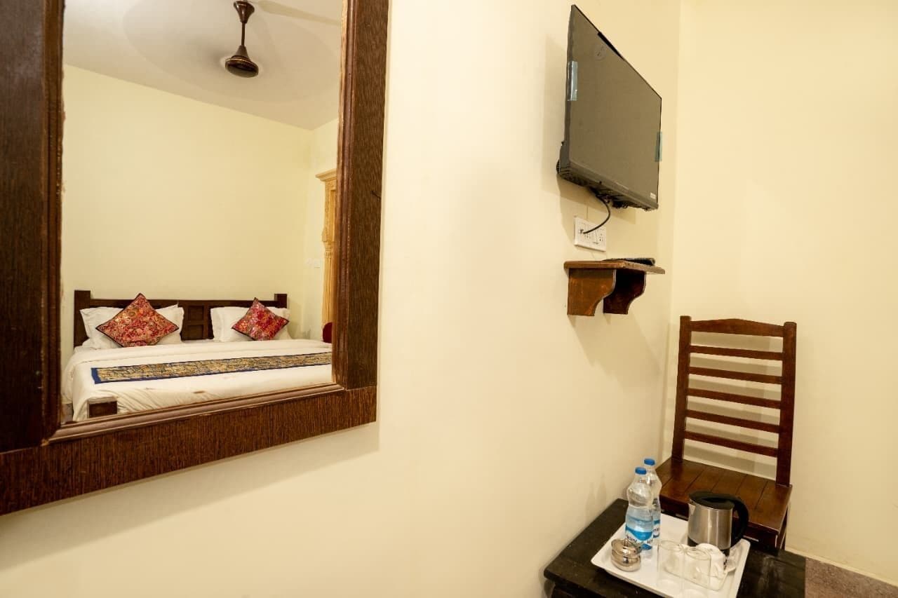 Ein Hotelzimmer mit einem Bett, einem an der Wand befestigten Fernseher, einem Holzstuhl und einem kleinen Tisch mit einer Wasserflasche und einem Wasserkocher.