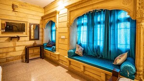 Quarto com um banco de madeira com almofadas azuis, um espelho e uma janela com cortinas azuis.