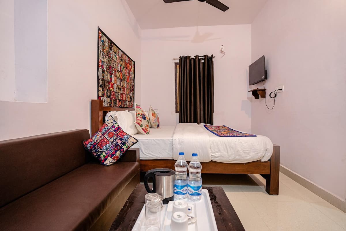 A small, cozy room with a bed, a sofa, a wall-mounted TV, and a ceiling fan.