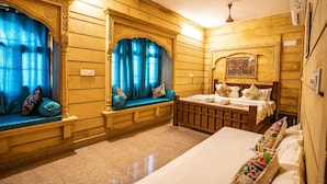 Quarto tradicional com cama, um banquinho com almofadas e janela com cortinas azuis.