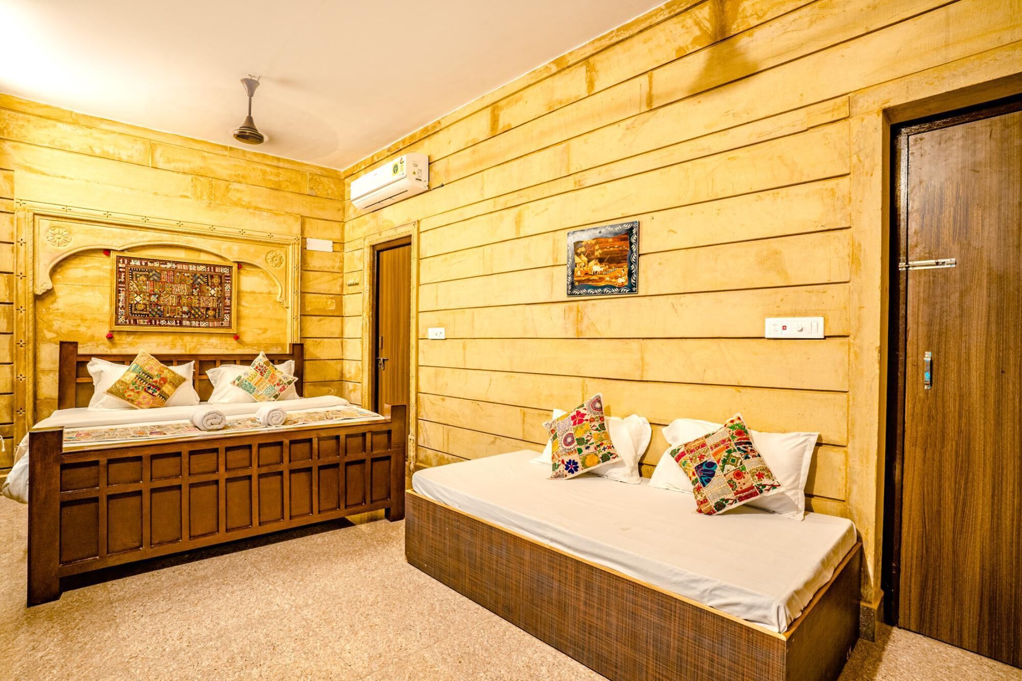 Una habitación con dos camas, paredes de madera, un ventilador de techo y un equipo de aire acondicionado, además de una puerta.