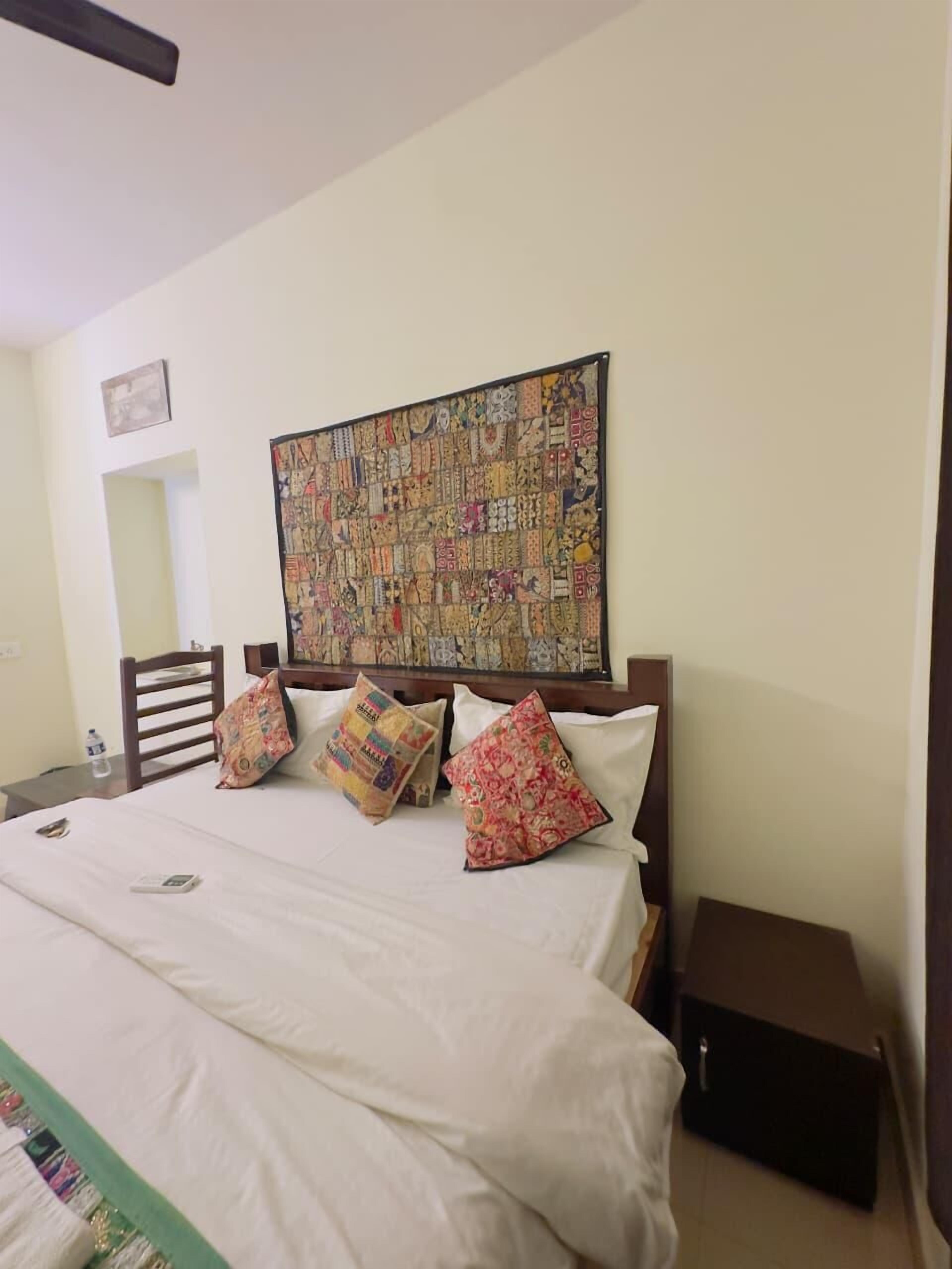 A hotel room with a large bed, a headboard with a colorful tapestry, and a small bedside table.