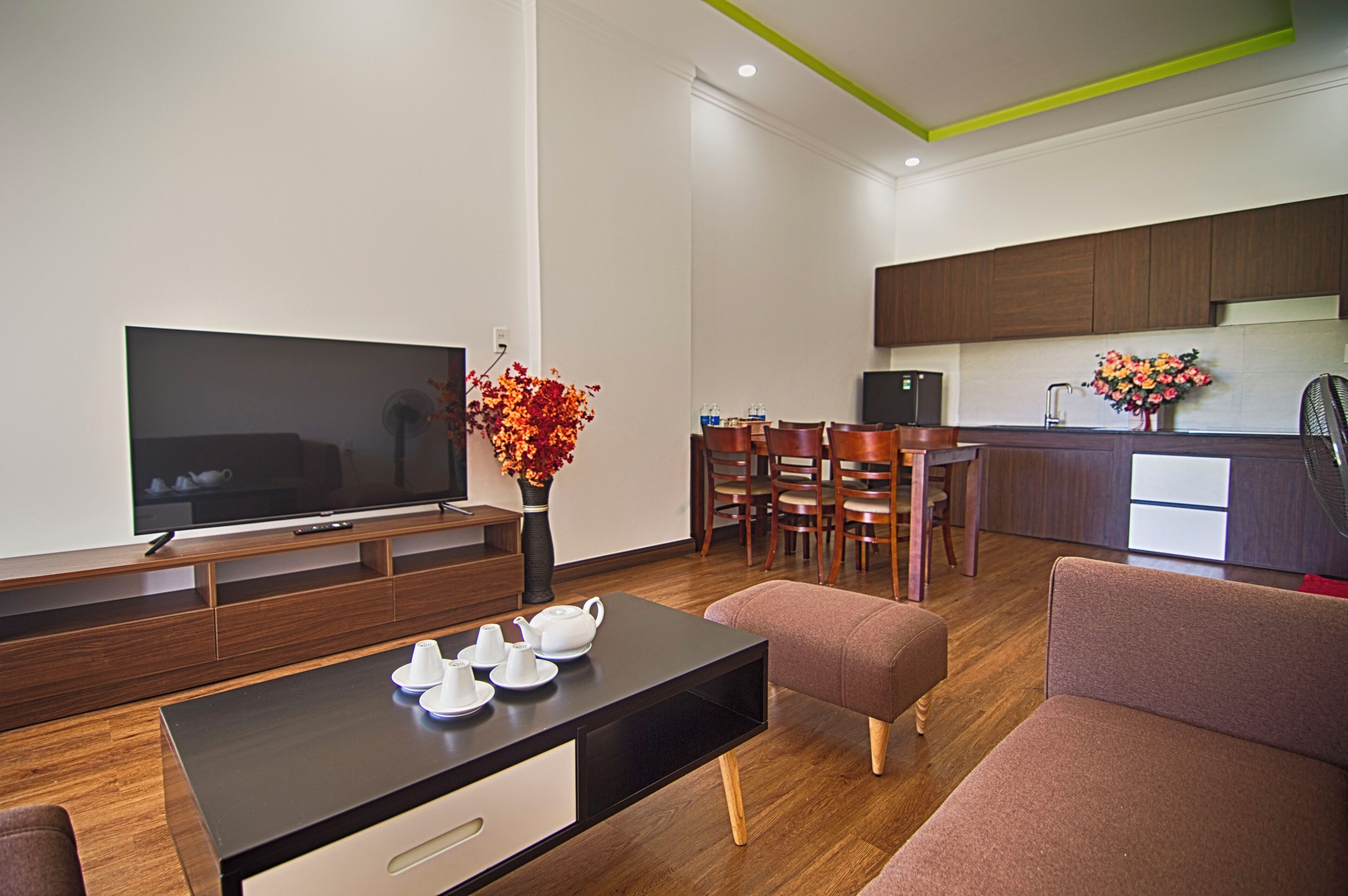 A modern living room with a flat-screen TV, a coffee table with cups, a sofa, and a dining area with chairs and a table.