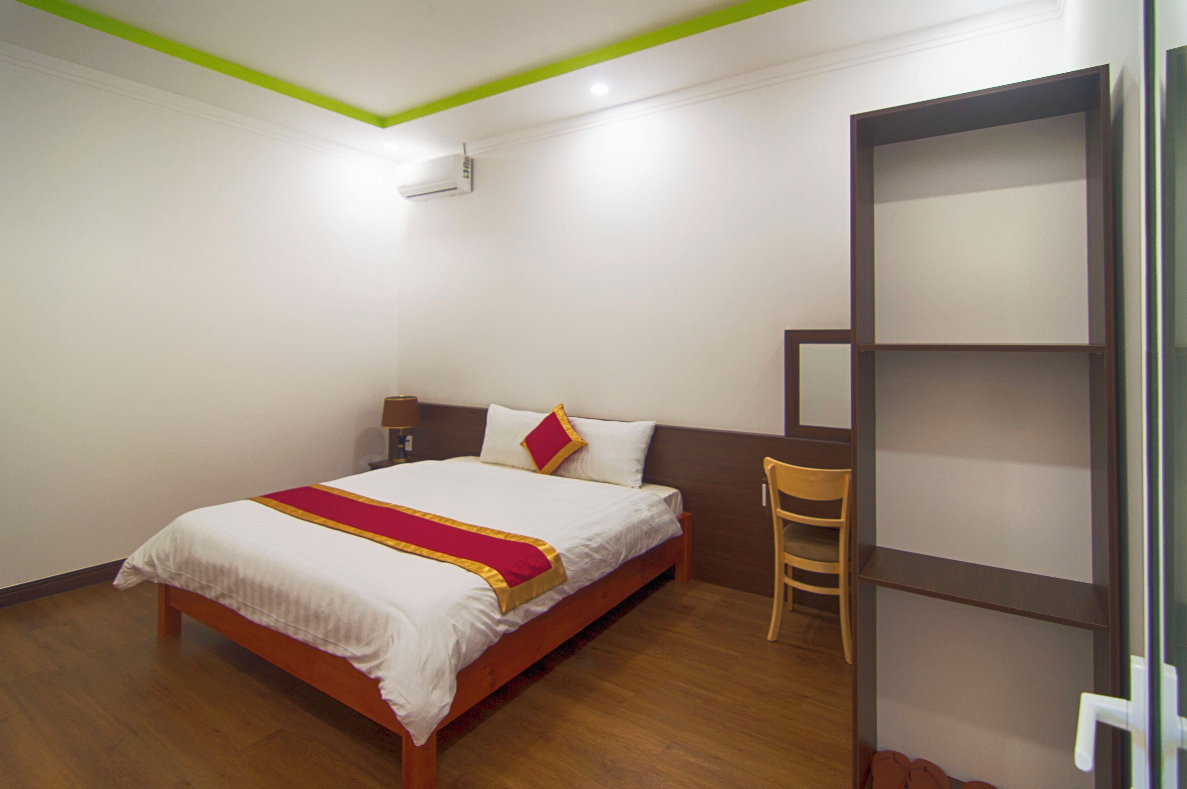 A hotel room with a wooden bed, a chair, a desk, and a bookshelf.