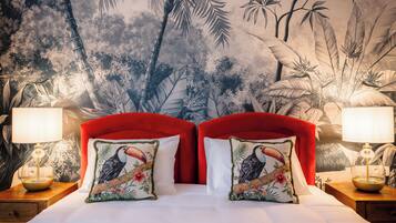 Un letto con testiera rossa, due cuscini con motivi floreali e un comodino con una lampada, oltre a un affresco vegetale sul muro.