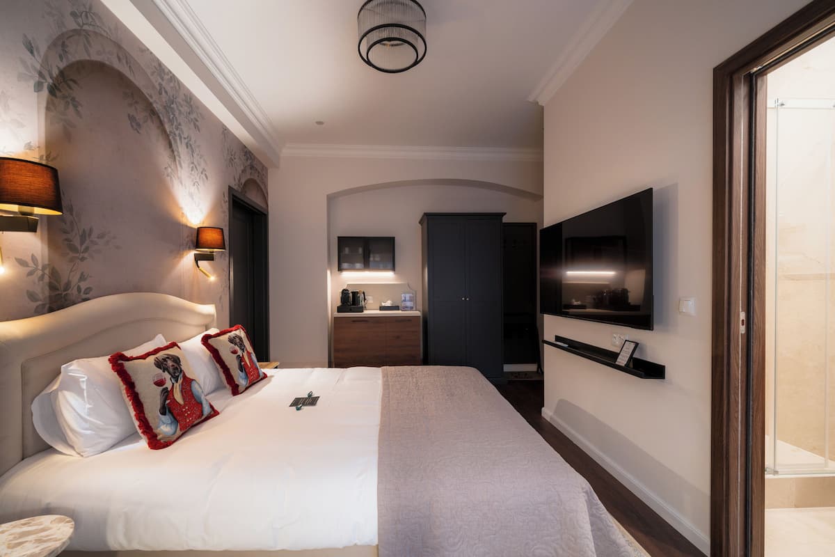 A hotel room with a bed, a TV, a desk with a coffee maker, and a wardrobe.