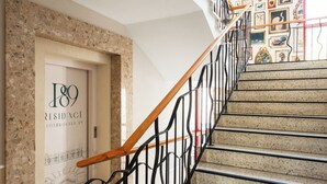 Un escalier doté d’une main courante en bois et d’une rampe en métal noir, menant à une porte portant l’inscription « Résidence 189 ».
