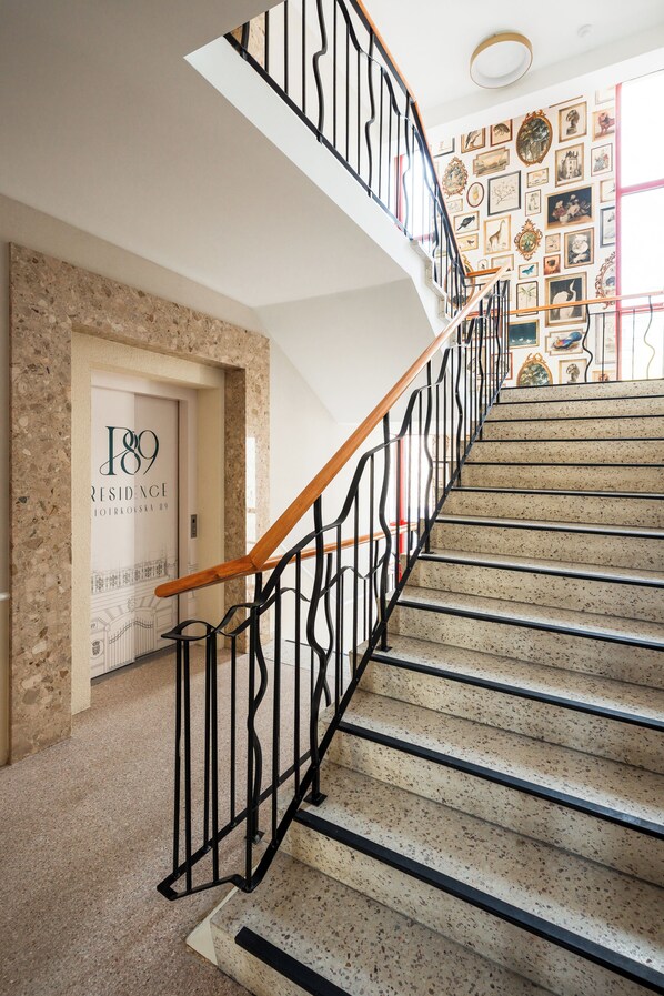 Escadaria com corrimão de madeira e guarda-corpo de metal preto, conduzindo a uma porta com a inscrição '189 Residence'.