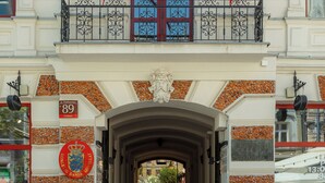 Une façade d’immeuble ornée de deux grands drapeaux rouges, un balcon avec des balustrades en fer forgé et une enseigne indiquant le numéro « 89 ».
