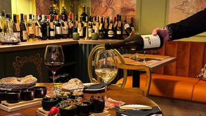 Un restaurant avec un comptoir où sont exposées différentes bouteilles de vin, une sélection de pains et d’olives sur la table, et un menu présenté sur la table.
