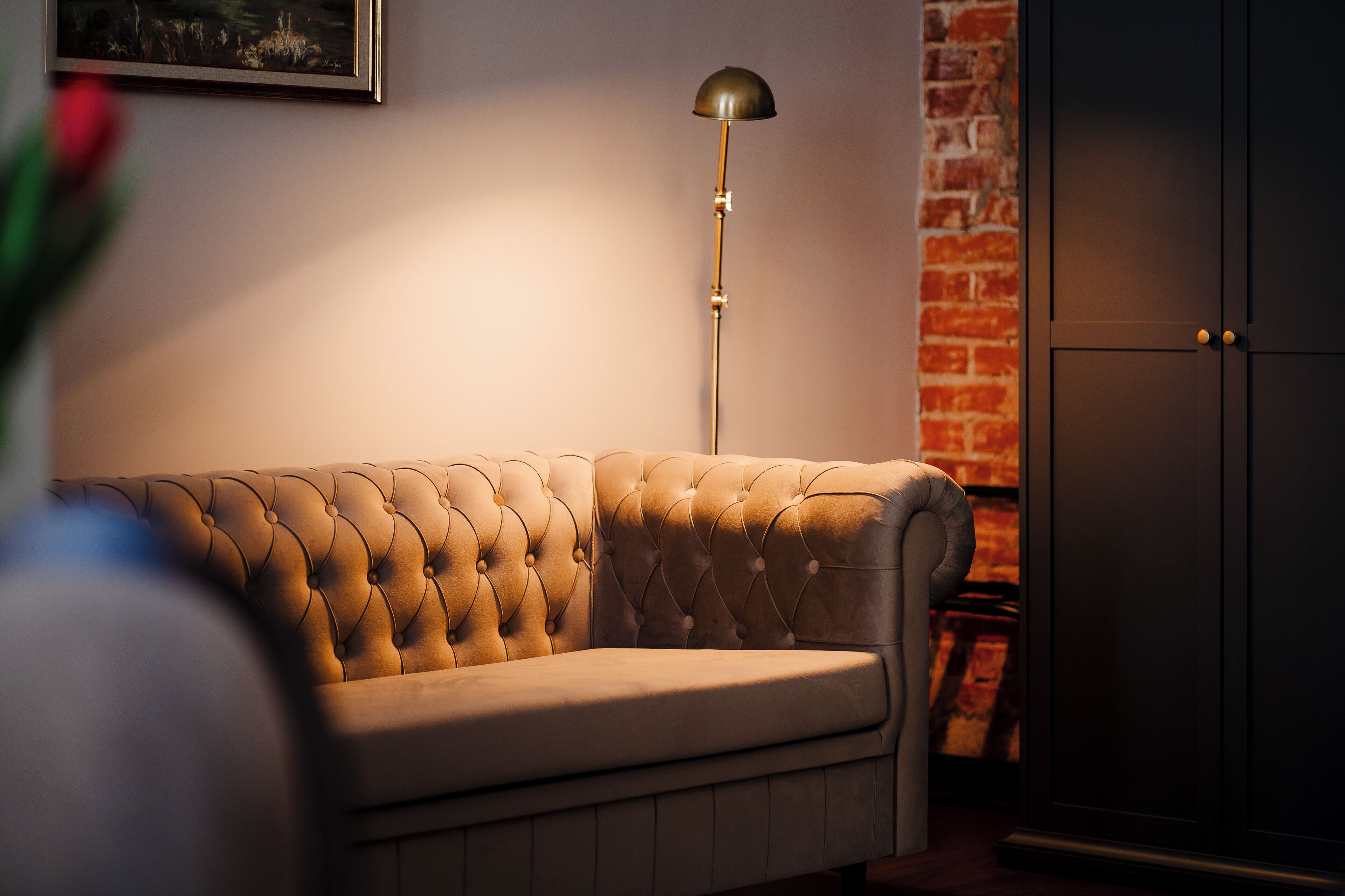 A tufted sofa in a room with a brick wall and a dark door.