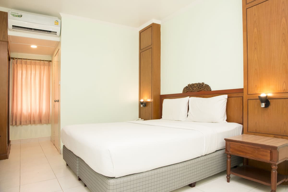 Une chambre d’hôtel comprenant un lit, une table de chevet, une armoire en bois et un appareil de climatisation.