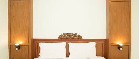 A hotel room with a wooden headboard, two bedside lamps, a telephone, and a bed with white bedding.