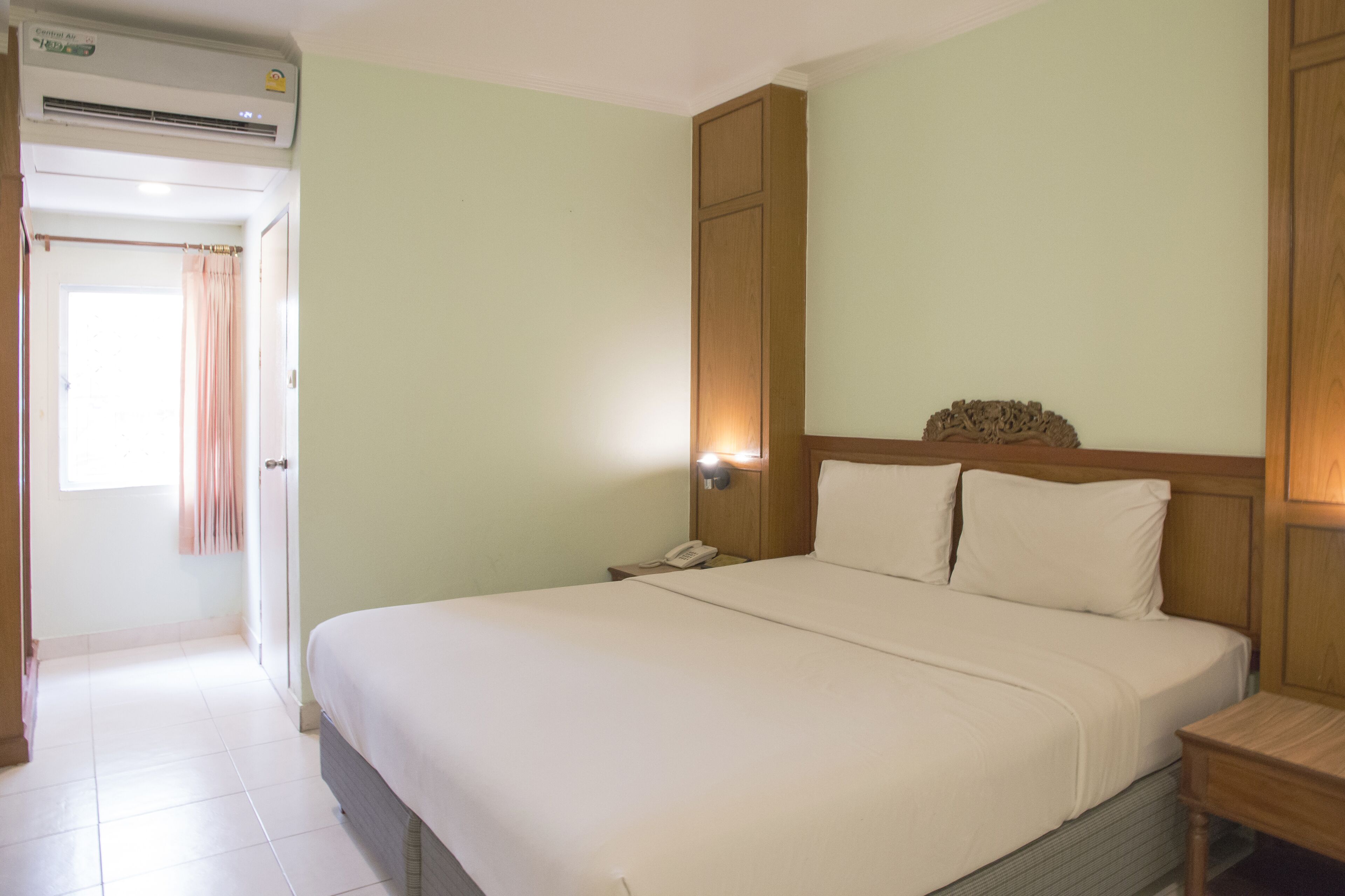 A hotel room with a bed, bedside table, and an air conditioning unit.
