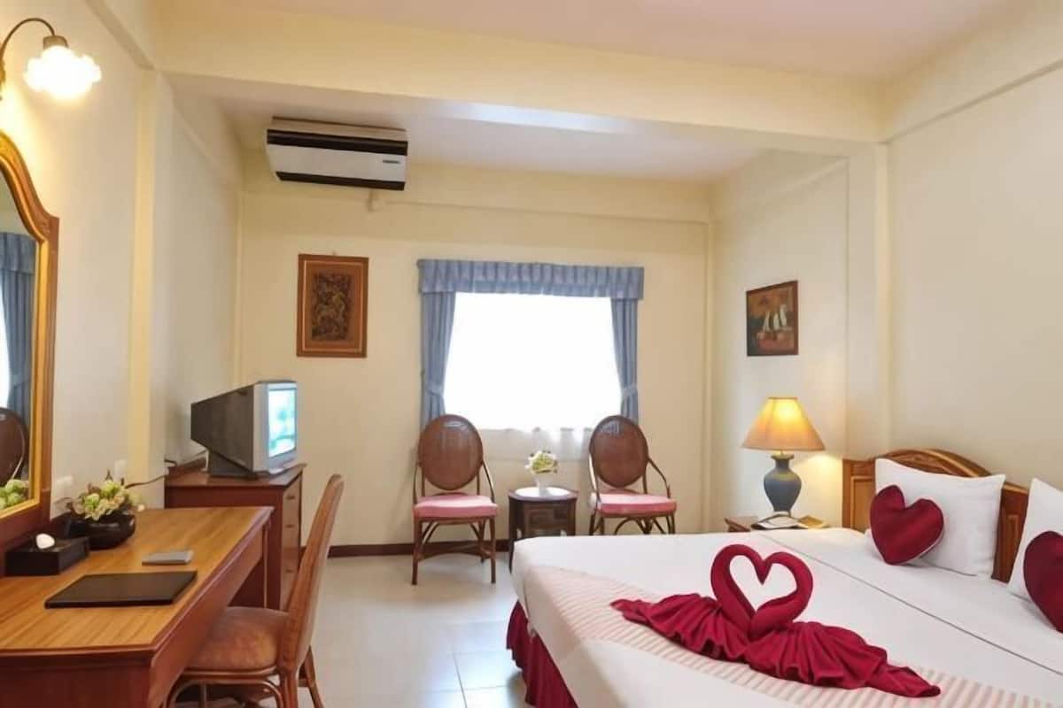 Une chambre d’hôtel avec un lit, deux chaises, un bureau avec un ordinateur, une télévision et une lampe.
