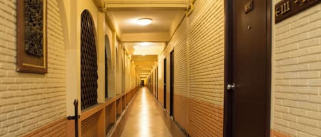 Un pasillo largo y estrecho con suelo de baldosas, paredes de ladrillo y puertas a un lado.