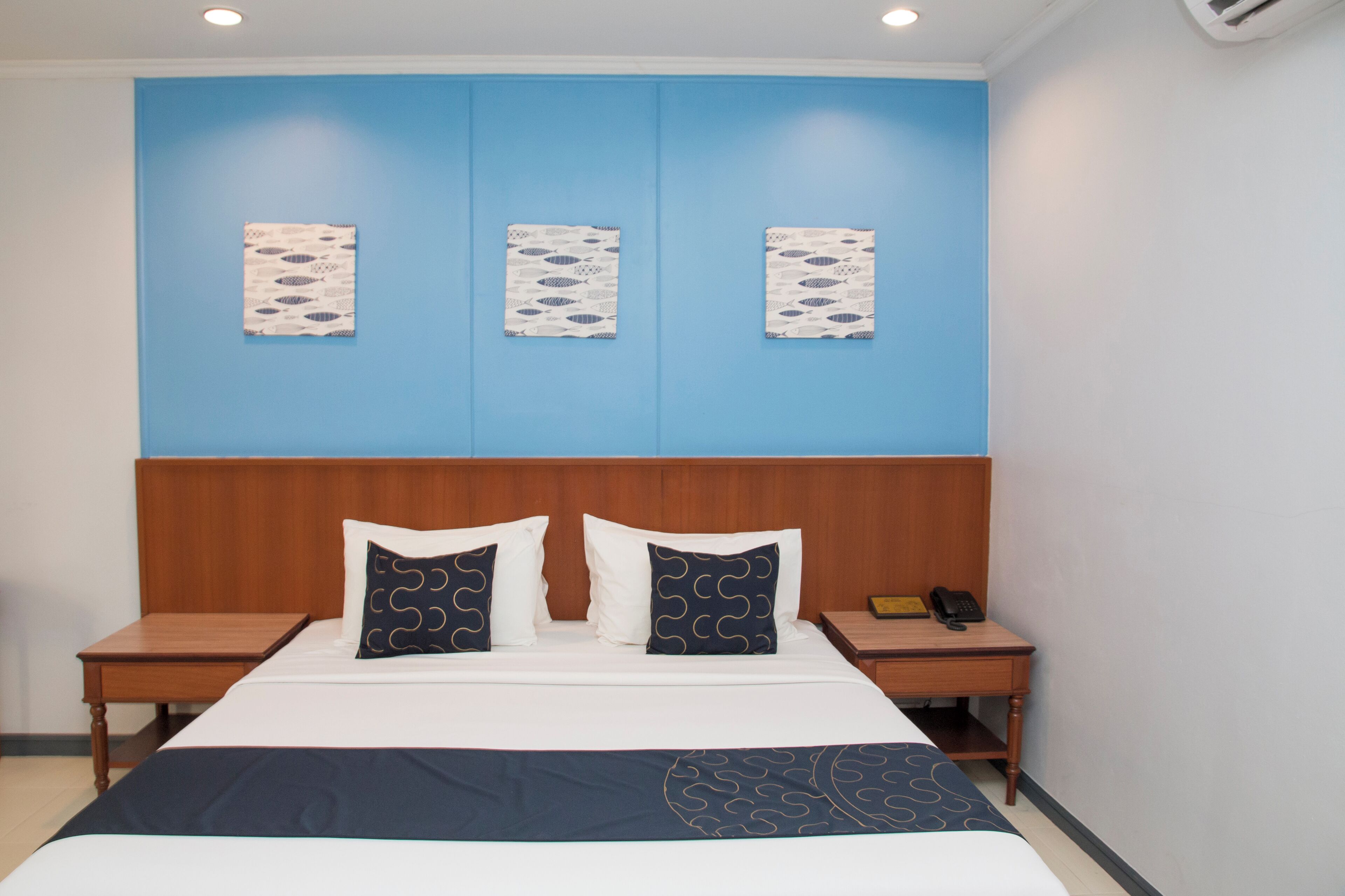 Habitación de hotel con cabecera de madera, cama con almohadas estampadas y tres obras de arte colgadas en la pared.