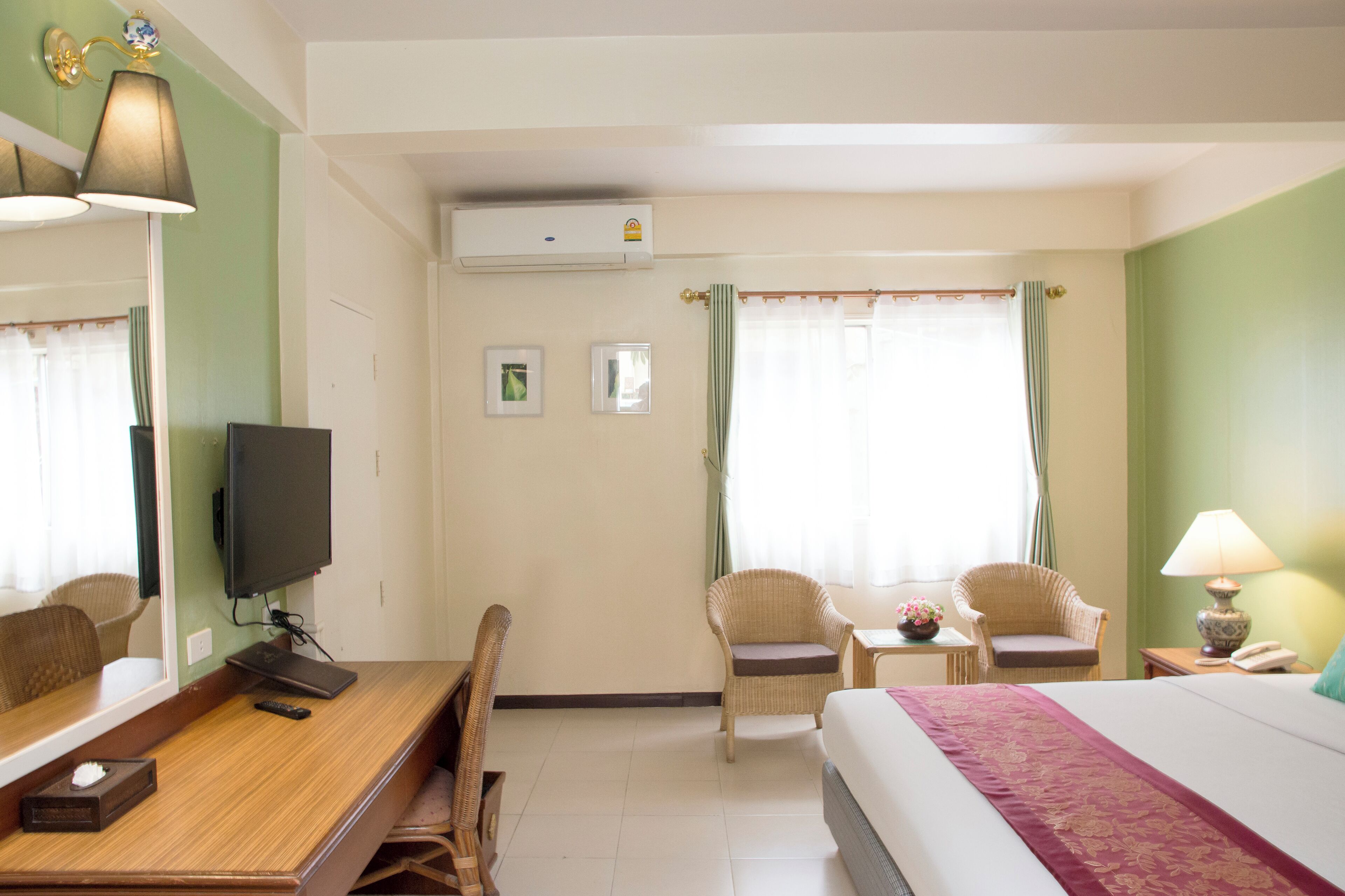 A hotel room with a bed, two chairs, a desk with a television, a lamp, and an air conditioning unit.