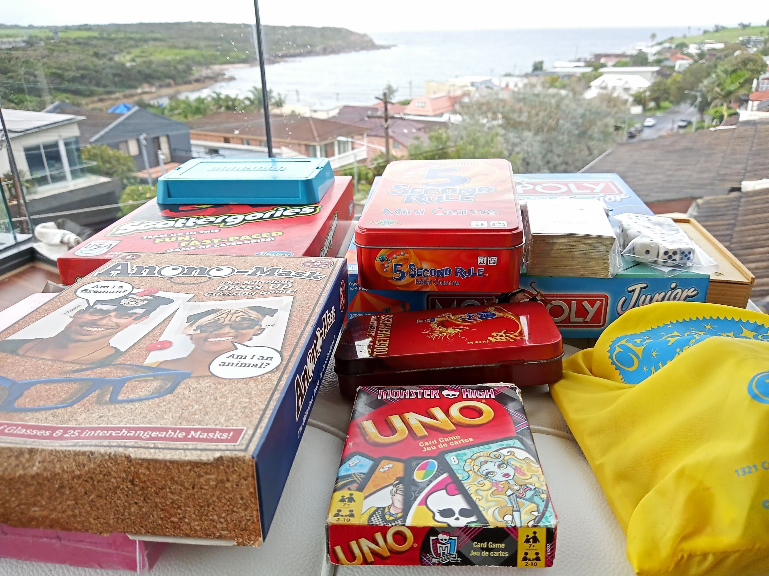 Une variété de jeux de société et de jouets sont disposés sur une table, avec en arrière-plan une vue panoramique d’une région côtière.