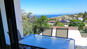 Un balcón con mesa y sillas, con vista a un pueblo costero con casas y al mar.