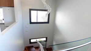 Un interior moderno con una escalera, una lámpara colgante y un ventanal con persianas.
