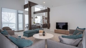 Una sala de estar moderna con un televisor grande, sofás grises y una mesa de centro redonda.