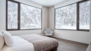 A modern bedroom with a large bed, two windows, a chair, and a nightstand. - Song Saa (Niseko)