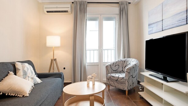 Un salon comprenant un canapé, un fauteuil, une télévision, une lampe et une petite table.