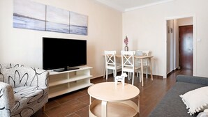Un salon équipé d’un téléviseur à écran plat, d’un canapé, d’une table ronde et d’un coin repas avec des chaises.