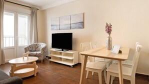 Un salon comprenant un téléviseur, une table à manger, des chaises, un canapé et une fenêtre avec des rideaux.