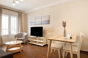 Una sala de estar con televisor, una mesa de comedor, sillas, un sofá y una ventana con cortinas.