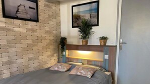 A bed with a headboard, a brick wall, a framed picture, and a door. - Studio Apartment 'La Noisette' with Private Terrace, Private Garden and Wi-Fi (Equemauville)