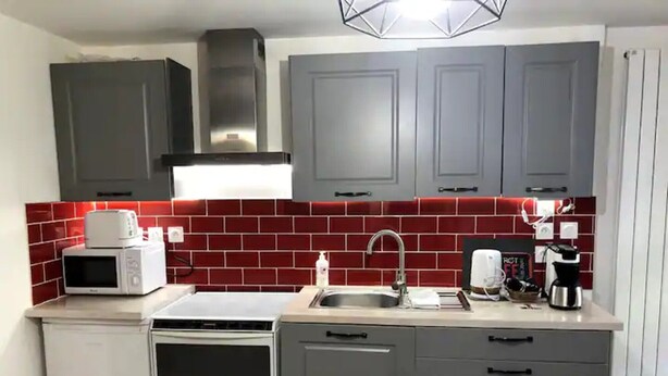 A compact kitchen with grey cabinets, a red-tiled backsplash, a microwave, a coffee maker, and a sink. - Studio Apartment 'La Noisette' with Private Terrace, Private Garden and Wi-Fi (Equemauville)