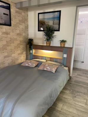 A bed with a headboard, a wall-mounted picture, and a potted plant. - Studio Apartment 'La Noisette' with Private Terrace, Private Garden and Wi-Fi (Equemauville)