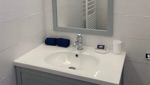 A bathroom with a white sink, a mirror, a towel rack, and a toilet paper holder. - Studio Apartment 'La Noisette' with Private Terrace, Private Garden and Wi-Fi (Equemauville)