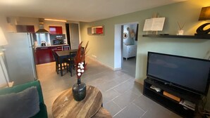 Ein modernes Wohnzimmer mit Fernseher, einem Essbereich und einer Küche im Hintergrund.