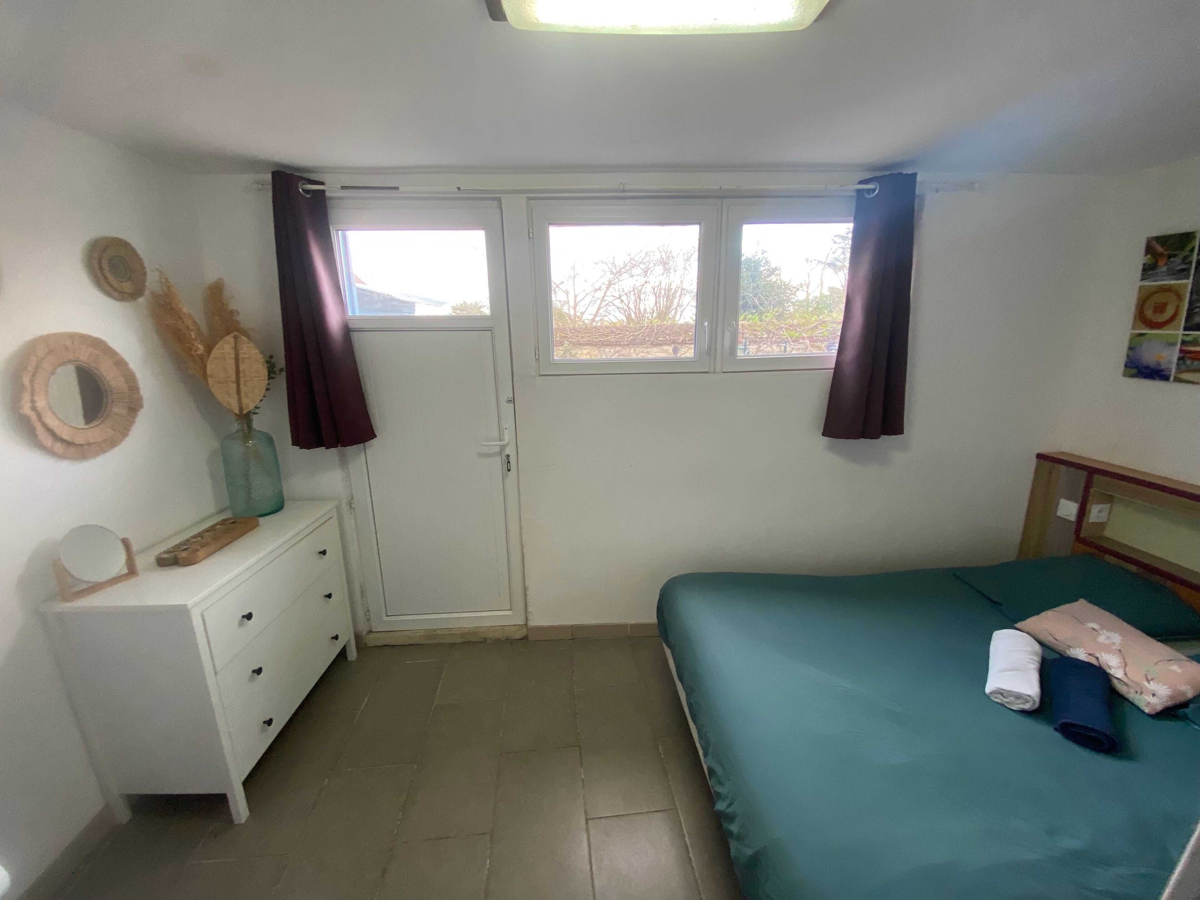 Ein Schlafzimmer mit Bett, Kommode, Fenster und Tür.