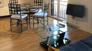 Un salon moderne avec une table à manger en verre, des chaises noires, un canapé, un téléviseur à écran plat et une grande fenêtre.