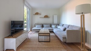 En moderne stue med et fladskærms-tv, en grå modulsofa, et træbord og en gulvlampe.