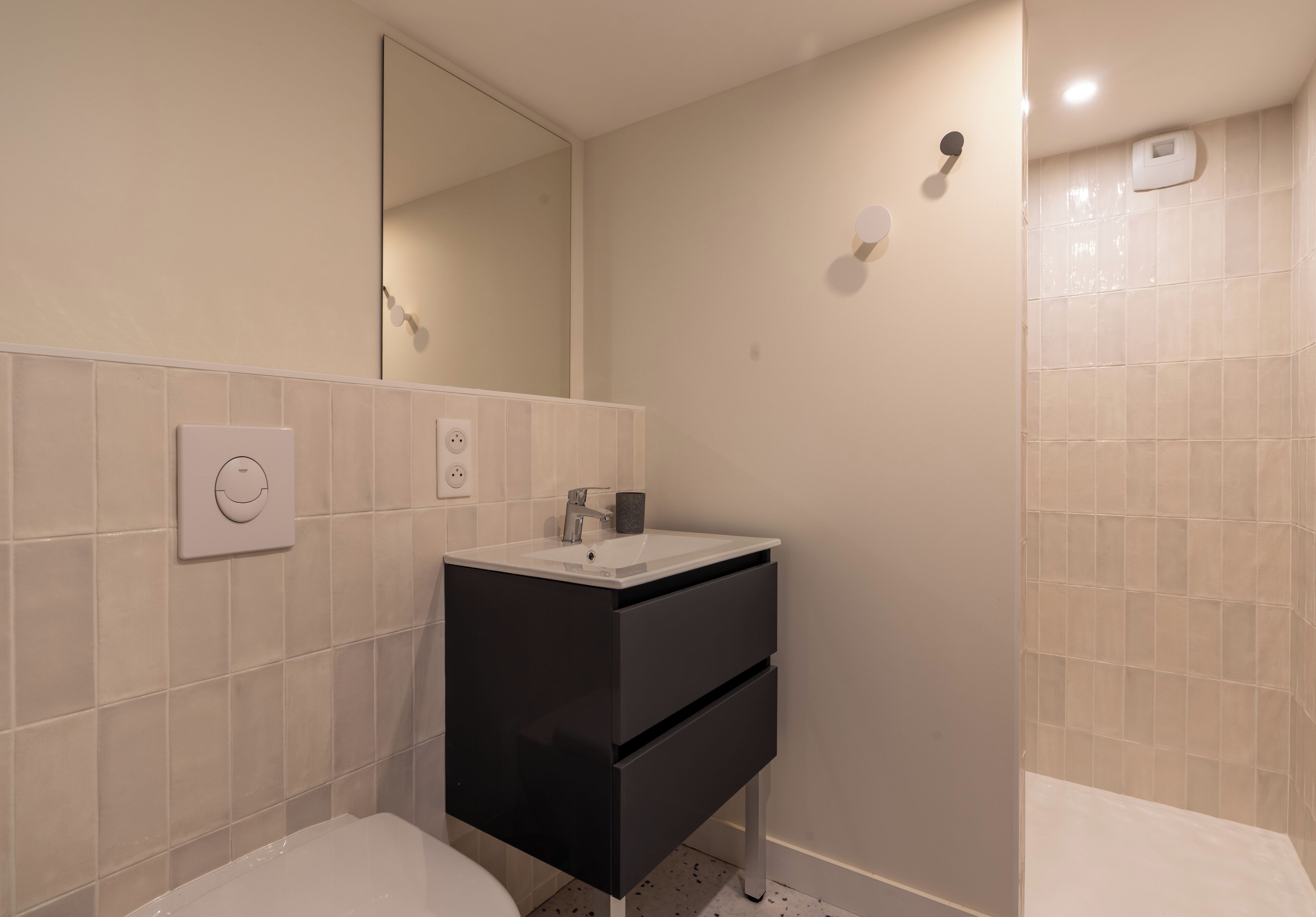 A modern bathroom with a white sink, black cabinet, and a large mirror.