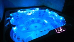 Un jacuzzi con múltiples chorros, iluminado con luces azules y un panel de control con pantalla digital.