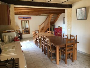 Un espace repas avec une table et des chaises en bois, une cuisine équipée d’une cuisinière et un escalier menant à un niveau supérieur.