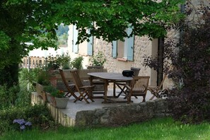 An outdoor patio with a wooden table and chairs, surrounded by potted plants and a stone wall. - Country House "Hameau Des Oraisonis" with Mountain View, Private Pool & Wi-Fi (Bras-d'Asse)
