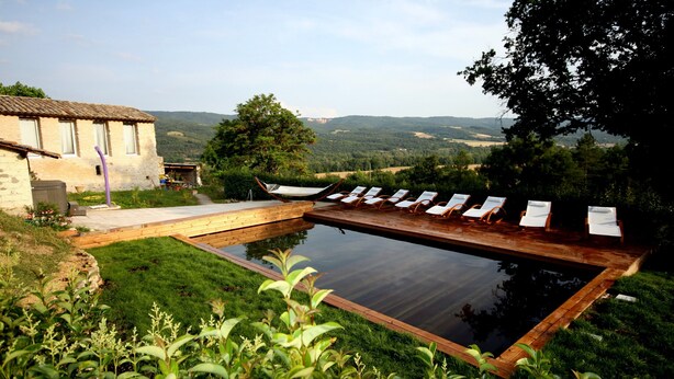 Una piscina con sillas de descanso, un edificio de piedra y vistas al campo.