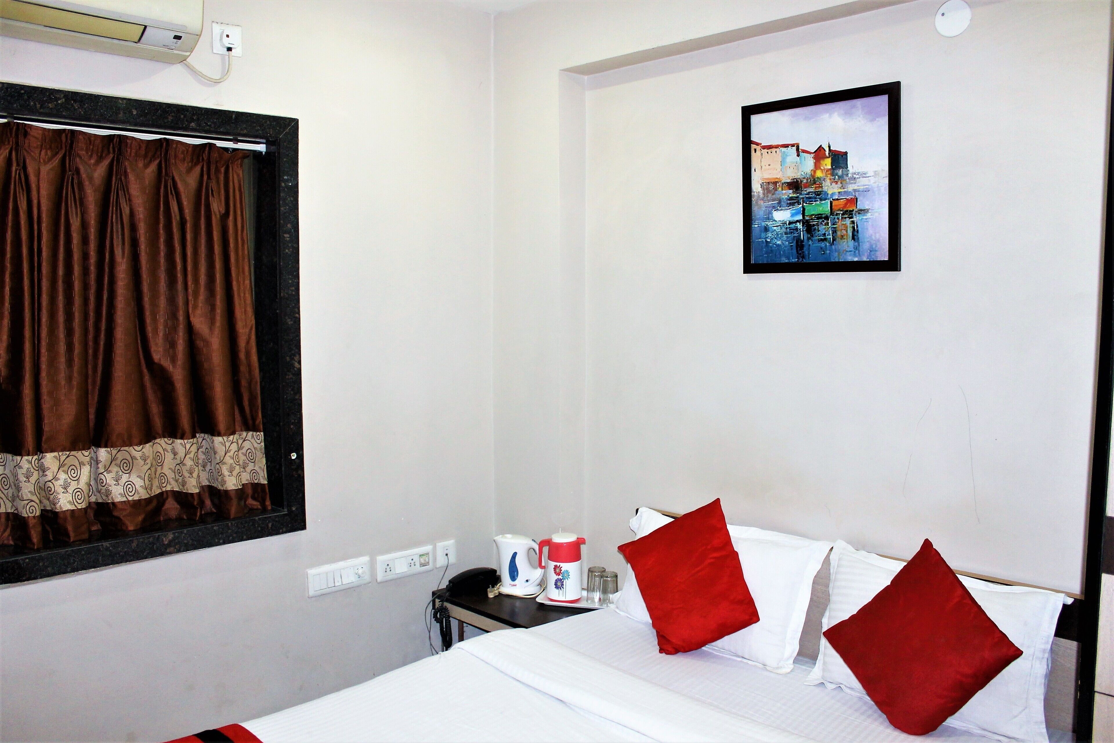Quarto de hotel com cama, mesa de cabeceira, cafeteira e um quadro na parede.