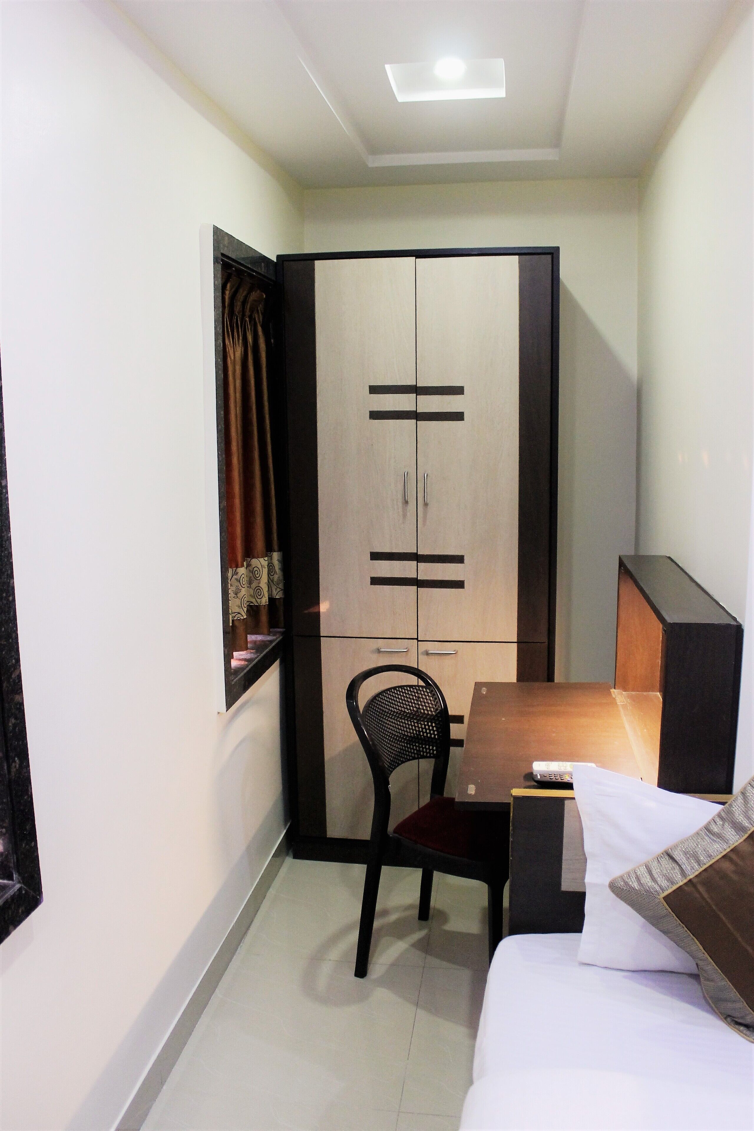 A small, modern room with a bed, a desk, a chair, a wardrobe, and a window with curtains.