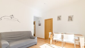 Sala de estar com um sofá cinza, uma mesa de jantar de madeira com cadeiras, uma porta de madeira e um sinal de WiFi fixado na parede.
